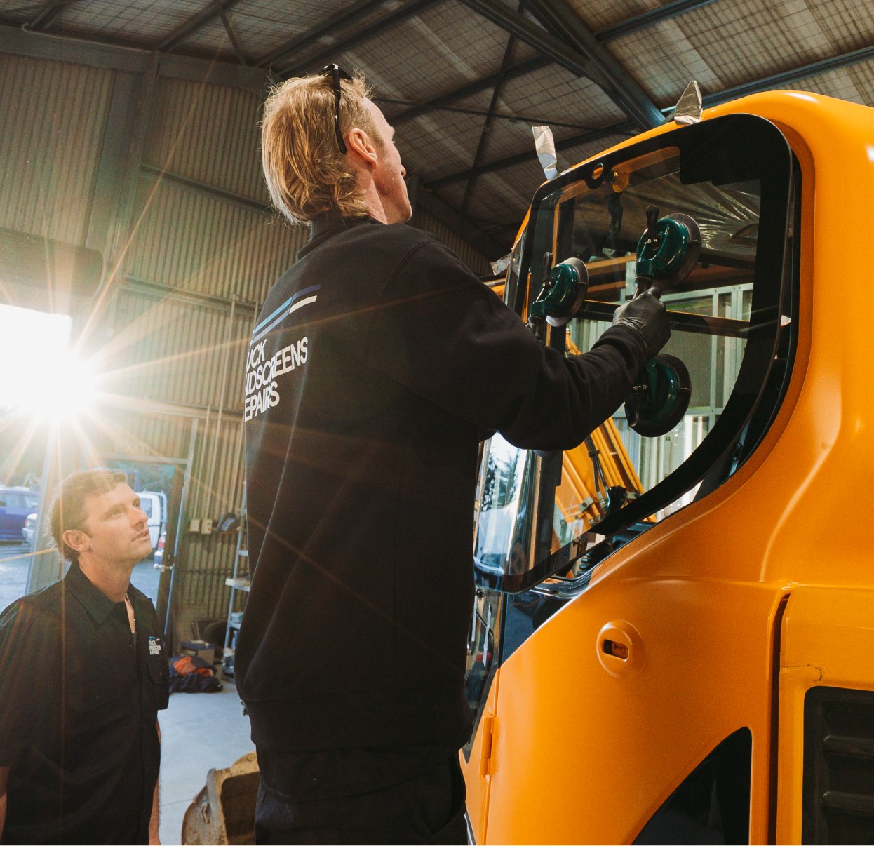Two technicians fitting glass to a machine cab